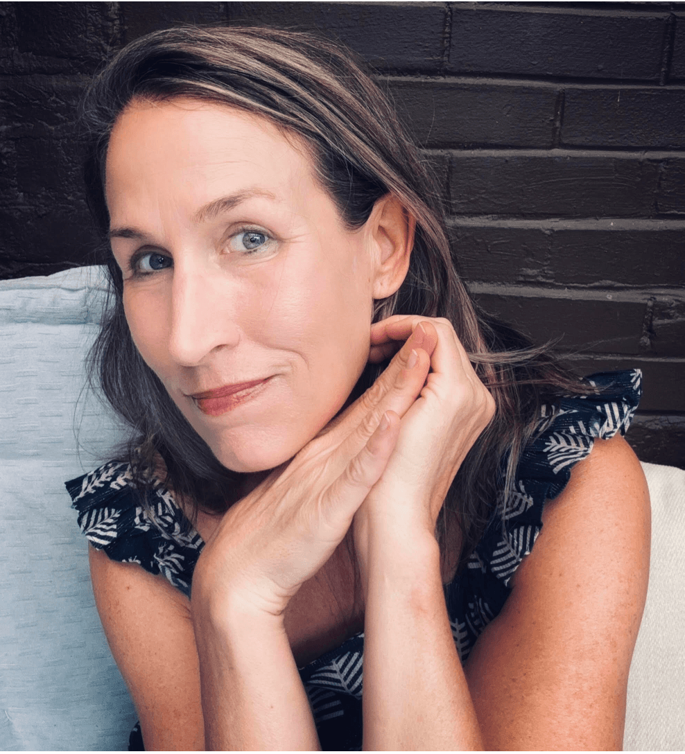 Portrait of Allison seated against a dark brick wall